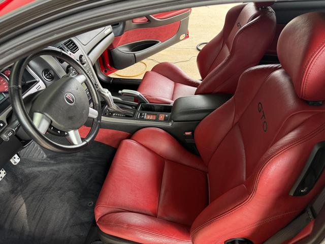 Red leather interior of a Pontiac GTO after detailing, with conditioned bucket seats and a polished center console