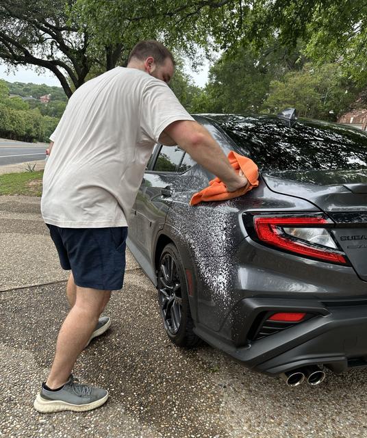 Kyle hand-drying a freshly washed 2025 Subaru WRX with an orange microfiber towel on an Austin driveway